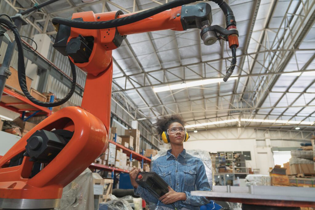 年轻的非洲裔美国女性工程师操作焊接机器人手臂在仓库工厂机器。专业技术人员自动化机械工业